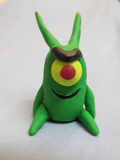 a green toy sitting on top of a white bed next to a red and yellow object