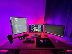 a desk with two monitors, keyboard and mouse on it in front of a purple wall