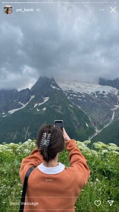 a woman taking a photo with her cell phone on top of a mountain in the mountains