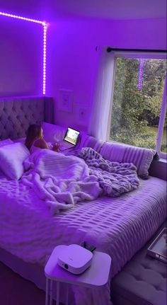 a woman laying in bed with a laptop on her lap and purple lights around her