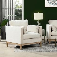 a living room with two white chairs and a lamp on the table in front of a green wall