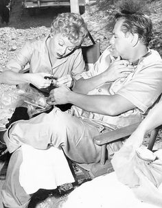 an old photo of two people sitting on a bench and one is cutting another persons hair