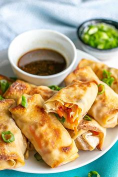 a white plate topped with wontons covered in cheese and vegetables next to dipping sauce