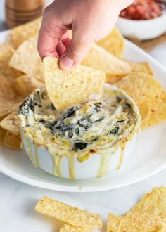 a hand dipping a tortilla chip into a bowl of spinach dip surrounded by chips