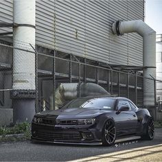 a black sports car parked in front of a building with a large pipe sticking out of it's side