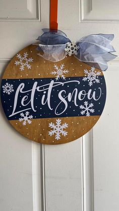 a wooden sign that says let it snow hanging on a door with ribbon and bow