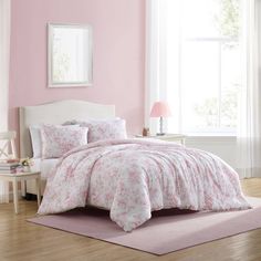 a white bed with pink flowers on the comforter and pillows in front of a window