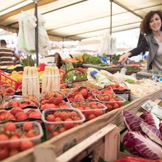 a woman standing in front of a table filled with lots of fruits and veggies