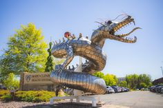 a large metal dragon statue sitting in front of a parking lot next to a building