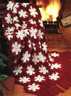 a red and white crocheted blanket sitting next to a fire place