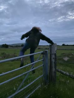 a man is jumping over a fence in the middle of an open field at dusk