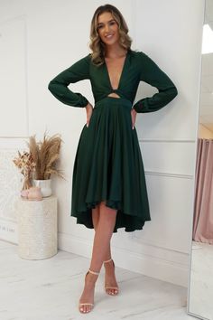 a woman standing in front of a mirror wearing a green dress with long sleeves and cut outs