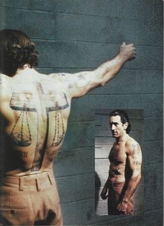 a man with tattoos on his back standing in front of a mirror next to a wall