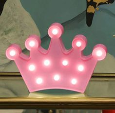 a pink light up crown sitting on top of a shelf in front of a painting