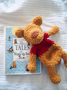 a crocheted teddy bear laying on top of a bed next to a book