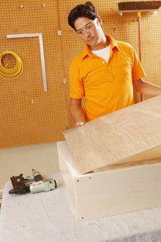 a man in an orange shirt is working on some plywood pieces with a hammer