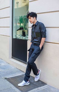 a young man leaning against a wall in front of a store window with his foot on the ground