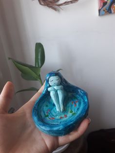 a hand holding a small ceramic figurine in the shape of a person sitting on top of a bowl