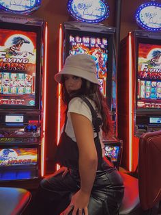 a woman sitting in front of slot machines with neon lights behind her and wearing a hat