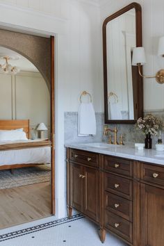 a bathroom with a large mirror and double sink vanity in front of a doorway that leads to a bed