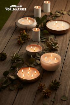 several lit candles sitting on top of a wooden table next to leaves and greenery