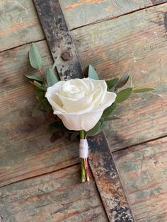 a boutonniere with a white rose on it sitting on a wooden surface