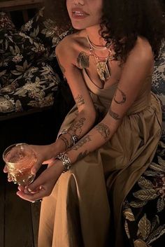 a woman with tattoos sitting on a couch holding a wine glass and looking at the camera