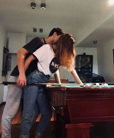 a man and woman kissing while standing in front of a table with a laptop on it