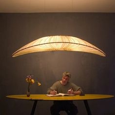 a man sitting at a table with a book in front of him under a lamp