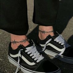 a person wearing black and white vans with tattoos on their feet, standing in the street