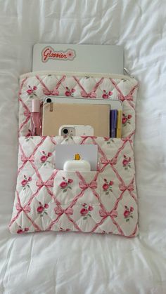 a white bed with a pink flowered bag on top of it and an electronic device in the pocket