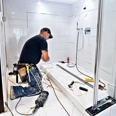 a man working on the floor in a bathroom with white tiled walls and tile floors