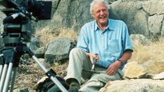 a man sitting next to a rock with a camera in front of him on a tripod