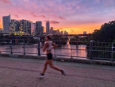 a woman running across a bridge with the city skyline in the background at sunset or dawn