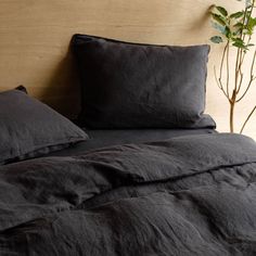 a bed with black linens and pillows on top of it, next to a potted plant