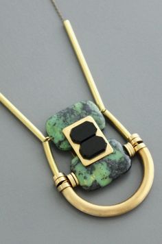 a green and black necklace with two gold rings hanging from it's sides on a gray surface