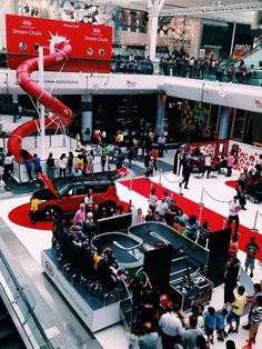 an indoor mall filled with lots of people and some red things in the middle of it