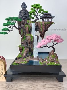 a bonsai tree with a waterfall and buddha statue in the middle on a wooden table