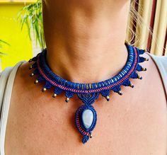 a woman wearing a blue and red beaded necklace with an oval shaped stone on it