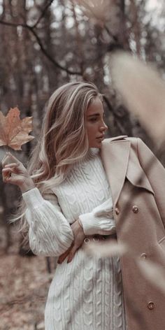 a woman in a white sweater and coat holding an autumn leaf