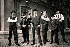 four men in suits and ties are standing on the sidewalk outside an old brick building