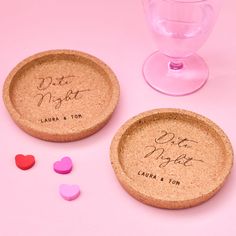 two personalized cork coasters sitting next to each other on a pink surface with hearts