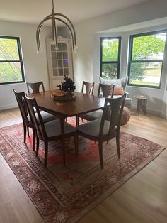 a dinning room table and chairs in front of two windows with large rug on the floor