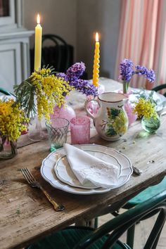 a wooden table topped with plates and cups filled with flowers sitting next to a lit candle