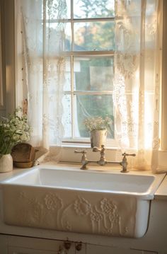 a white sink sitting under a window next to a potted plant and vase with flowers