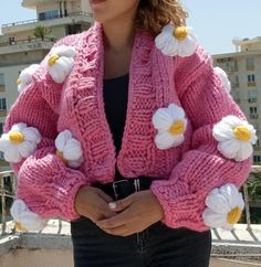 a woman standing in front of a building wearing a pink sweater with flowers on it