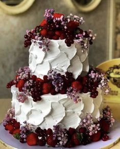 a three tiered cake with white frosting and red berries on top, sitting on a table