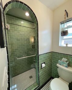 a bathroom with green tiles and a white toilet in the corner, next to a walk in shower