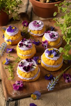 there are many desserts on the cutting board with purple and yellow flowers around them