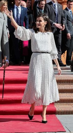 a woman in a white dress is walking down the red carpet with her hand raised